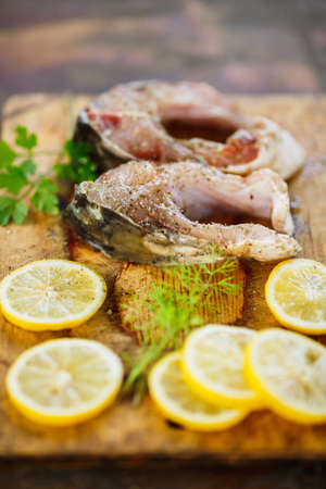 two  raw pieces of fish with slices of lemon  and green parsley on a wooden Board