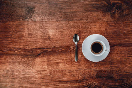 top view of white Cup with black coffee on a white saucer and teaspoon on dark brown wooden background  with space for  copytextの写真素材