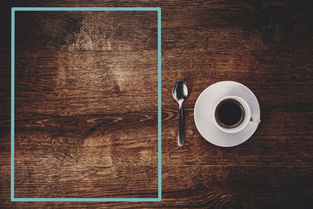 top view of white Cup with black coffee on a white saucer and teaspoon on dark brown wooden background with blue frame on the left for copy spaceの写真素材