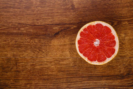 one red juicy slice of grapefruit on the wooden backround with copy space on the leftの写真素材