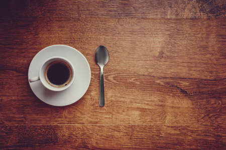top view of white Cup with black coffee on a white saucer and teaspoon on dark brown wooden background  with space for  copytext on the rightの写真素材