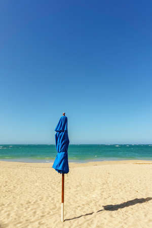 closed blue beach umbrella with shadow on the sandy beach on background of blue sea and skyの写真素材