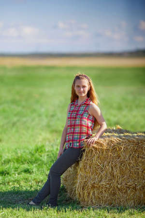 young cute teen girl posing near a haystack in the field. rural lifeの写真素材