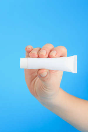 cream advertising, female hand holds the white cream tube with copy space on blue backgroundの写真素材