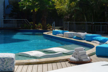 Luxury elite resort, relaxation place by the blue pool with daybeds, Ottomans and white towels