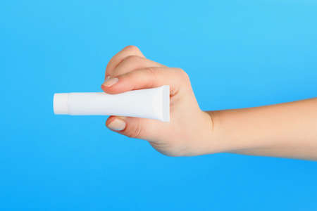 cream advertising, female hand holds the white cream tube with copy space on blue backgroundの写真素材