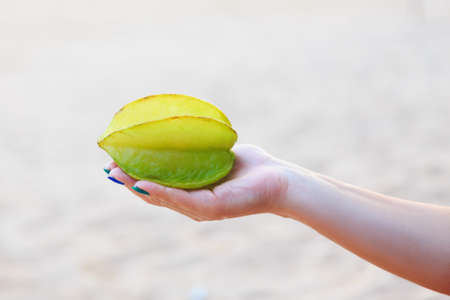 female hand giving the whole exotic yellow green carambola fruitの写真素材
