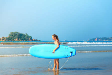 white blonde surfer girl in bikini with blue surfboard on the beachの写真素材