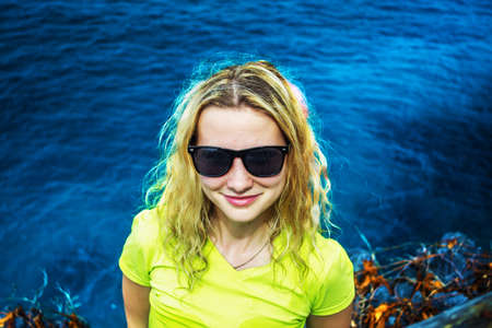Happy smiling girl with curly hair in sunglasses on background of dark blue caribbean seaの写真素材