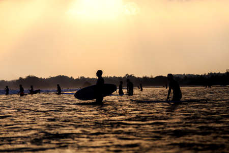 silhouettes of group of surfers in the ocean at sunset. Weligama, Sri Lanka