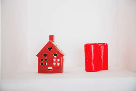red ceramic house and two red candles on white background