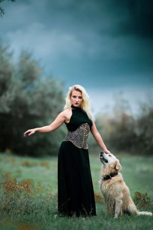 fashion girl model in long black dress and her dog golden retriever in gloomy day