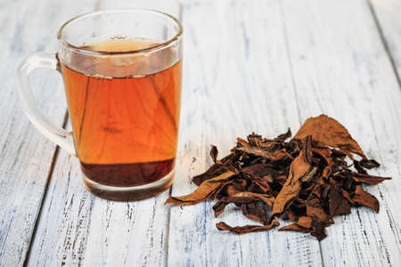 Cup of hot black tea and dried tea leaves on wooden tableの写真素材
