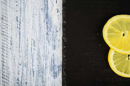two fresh lemon slices on a stone black board on light wooden background with copy space on left...