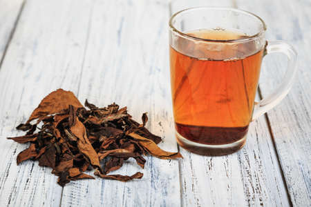 Cup of hot black tea and dried tea leaves on wooden tableの写真素材