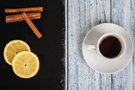 cup of hot coffe on rustic table and cinnamon sticks and lemon on black chalkboard, flat lay, top viewの写真素材