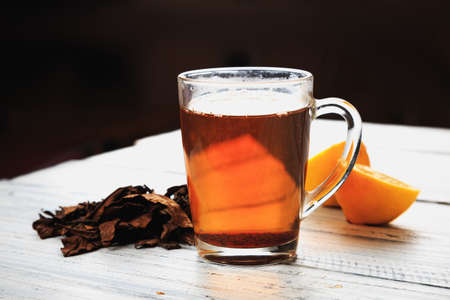 Cup of hot tea, dried tea leaves and lemon wedges on wooden tableの写真素材