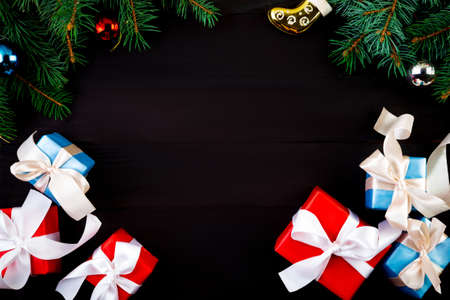 Christmas or new year frame, color wrapped presents, fir-tree branches and decorations on black background, flat layの写真素材