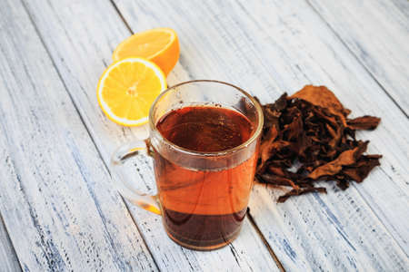Cup of hot black tea, dried tea leaves and citrus halves on a light wooden backgroundの写真素材
