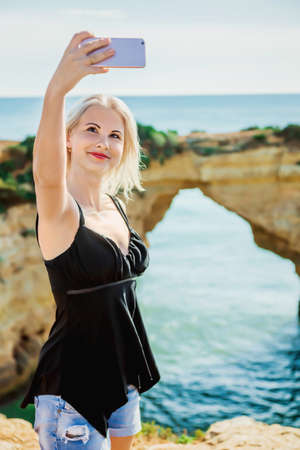 Happy young girl traveller make selfie on background of sea and cliffsの写真素材