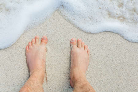 men's feet on sand near sea surf, vacation concept