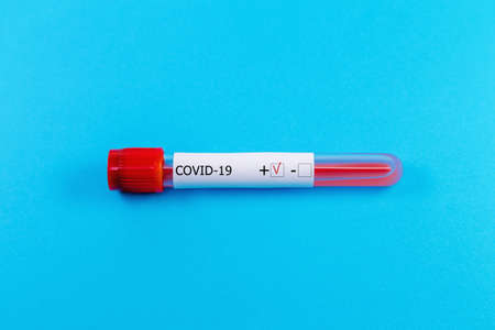 Positive COVID-19 blood tube test on blue background. Pandemic infectious concept
