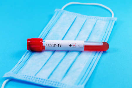 Protective medical mask with positive coronavirus blood tube test on blue background. Healthcare and medical concept. Coronavirus or COVID-19 protection concept.の写真素材