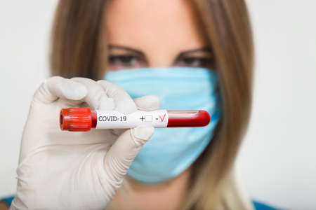 Nurse doctor in medical mask holding test tube with negative coronavirus test blood sample on blured backgroundの写真素材