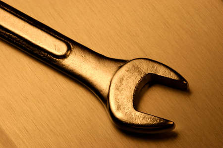 Steel wrench over a brushed steel surface with a warm light.