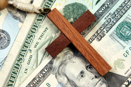 A wooden cross over a stack of money with the words in god we trust besides it.の写真素材