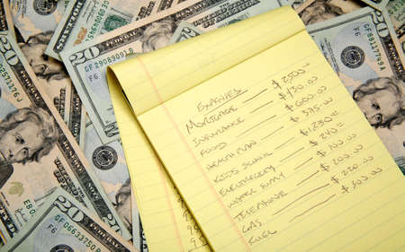Lots of cash, twenty dollar bills, disperse over a table top and a budget list.の写真素材