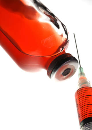Syringe and container with red fluid in a backlit setting for high key exposure and shallow depth of field.の写真素材