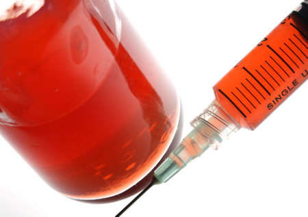 Syringe and container with red fluid in a backlit setting for high key exposure and shallow depth of field.の写真素材