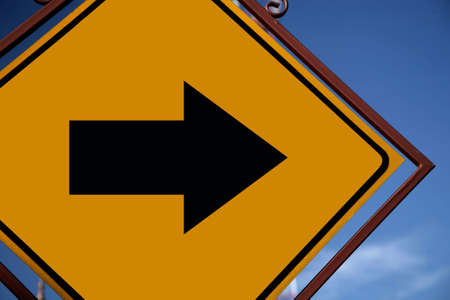 Arrow pointing direction on a yellow romboid road sign with an ornamental frame of bronze color.の写真素材