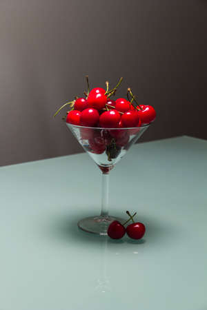 Photo of a martini glass full of cherries, with blurry background and two cherries near the stemの写真素材
