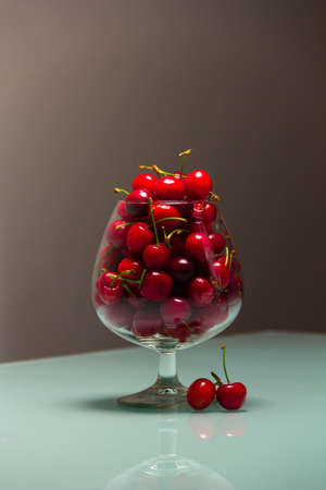 Photo of a glass full of cherries, with blurry background and two cherries near the stemの写真素材