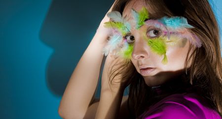Beautiful girl with colorful feather on her faceの写真素材
