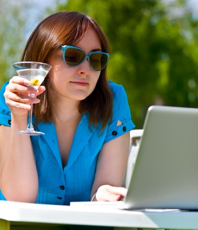 Businesswoman with laptop and glass of martini outdoorsの写真素材
