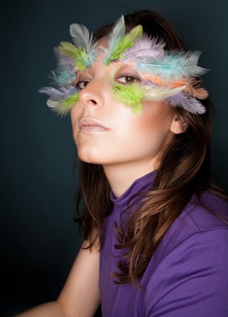 Beautiful girl with colorful feather on her faceの写真素材