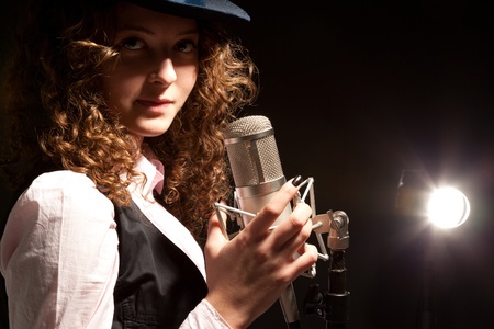 Picture of beautiful singer in hat with microphone on the black backgroundの写真素材