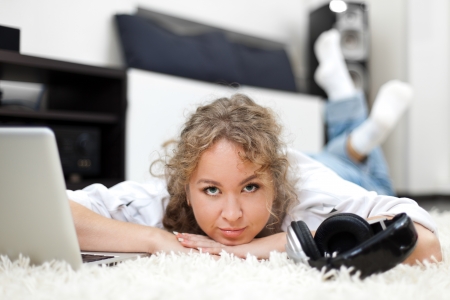 Beautiful woman with laptop and headphones lying on the carpetの写真素材