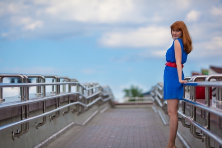 Beautiful woman in blue dress and red belt standing on the bridgeの写真素材