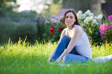 Beautiful brunette woman in white t-shirt sitting on the grass and relaxingの写真素材