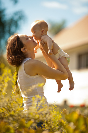 Happy woman holding in arm a laughing baby near houseの写真素材