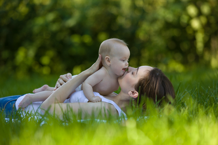 Happy woman holding in arm a baby in a garden and lying on the grassの写真素材