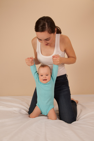 Cheerful mother with baby in blue bodysuit playing in bed and having funの写真素材