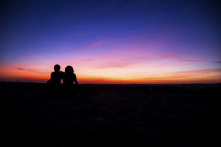 Silhouettes of lovers men and women stand on the background of sunset skyの写真素材
