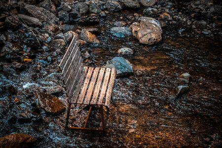 The wooden chair is set in a rocky stream filled in the forest.の写真素材