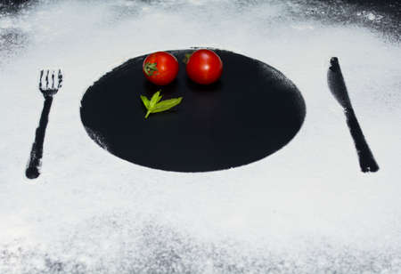 On a black marble background flour powder powdered snow silhouette plate plate fork knife appliances in the center tomato and mintの写真素材