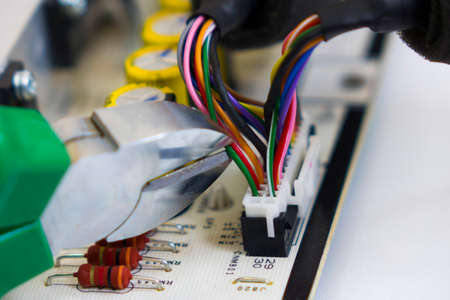 Dismantling electronic bomb, tongs cut the red wire into a bundle of colored wires on the background...